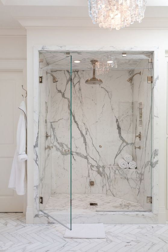 a bathroom with marble walls and flooring, chandelier above the shower area