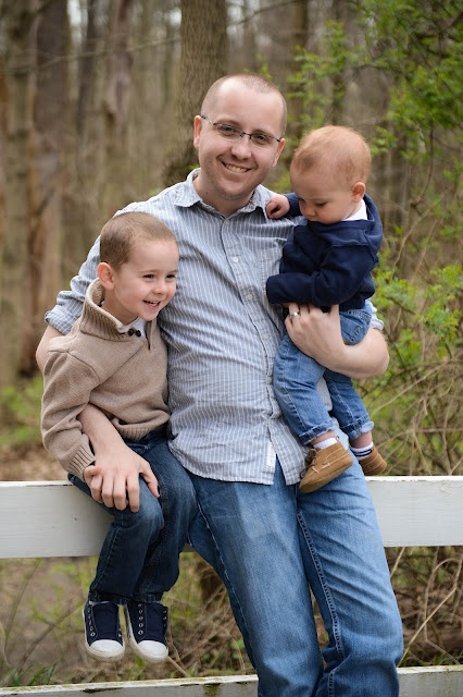 a man is holding two young boys while posing for a photo in front of some trees