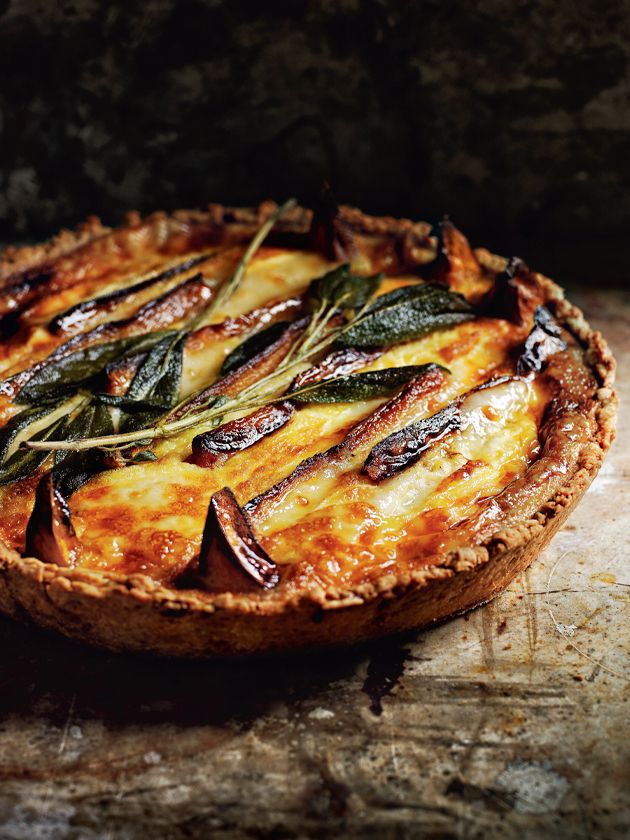 a quiche with cheese and greens on a wooden table next to a stone wall