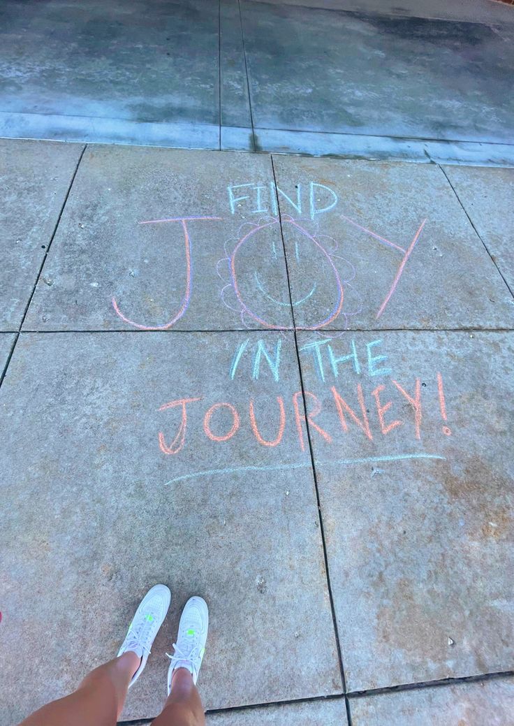 someone's feet on the sidewalk with chalk writing that says find joy in the journey