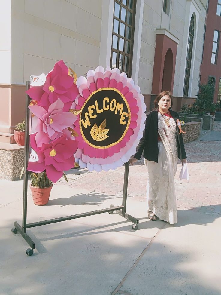 a woman standing in front of a welcome sign with flowers on it and the words welcome