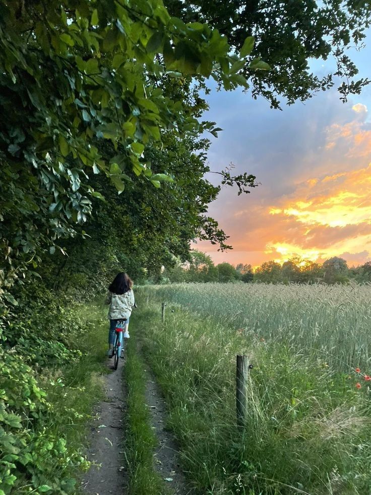 a person riding a bike down a dirt road next to tall green grass and trees