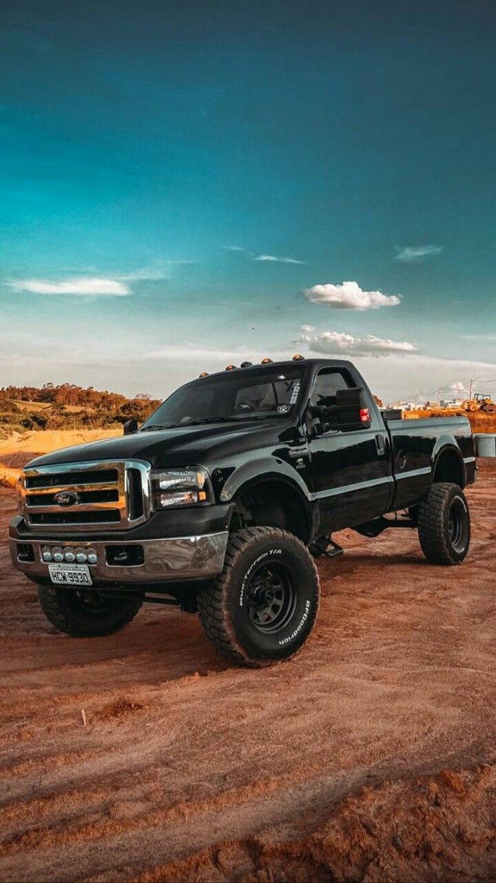 a large black truck parked on top of a dirt field