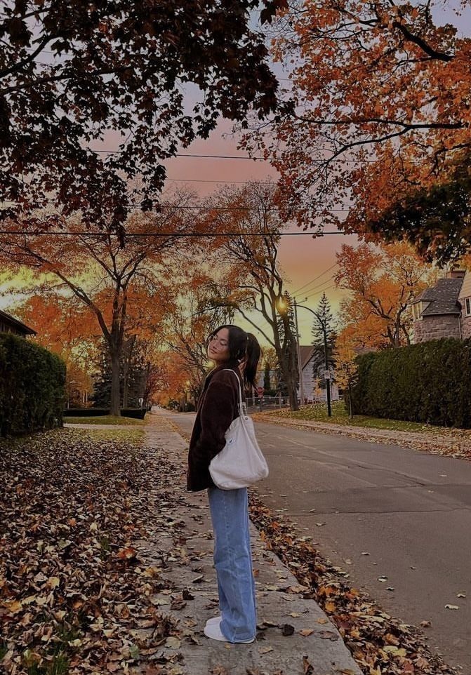 a woman standing on the side of a road with her hand in her pocket and looking up into the sky