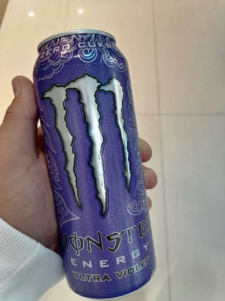 a person holding up a purple monster energy drink