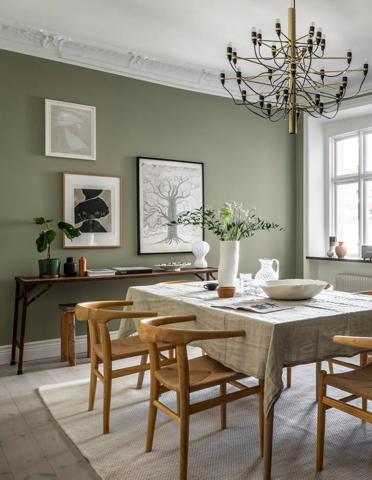 a dining room with green walls and wooden chairs, a chandelier and pictures on the wall