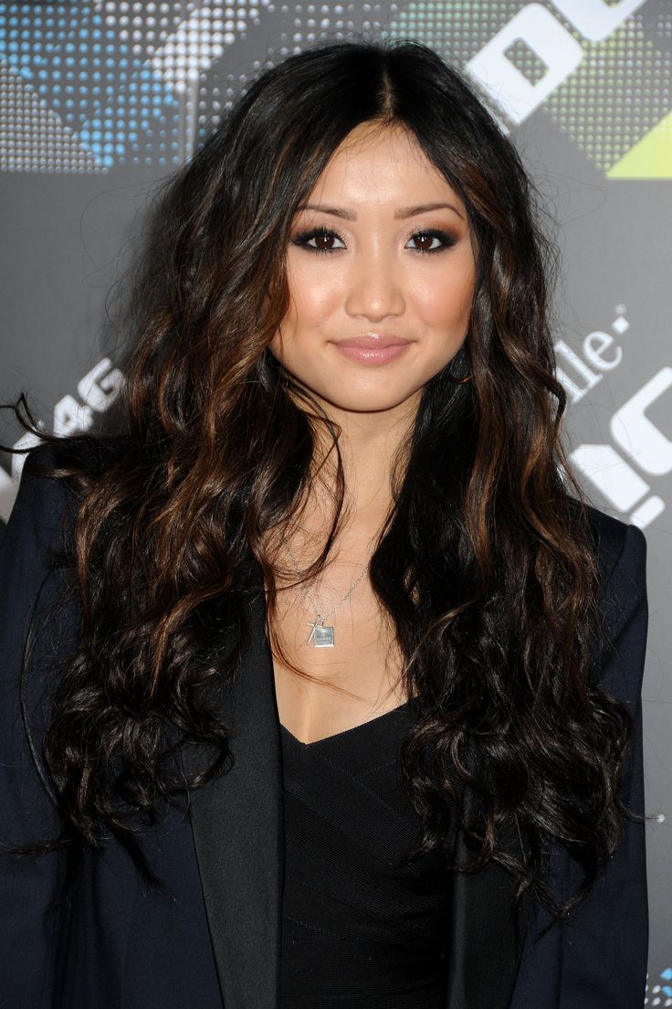 a woman with long dark hair smiling at the camera and wearing a blazer jacket