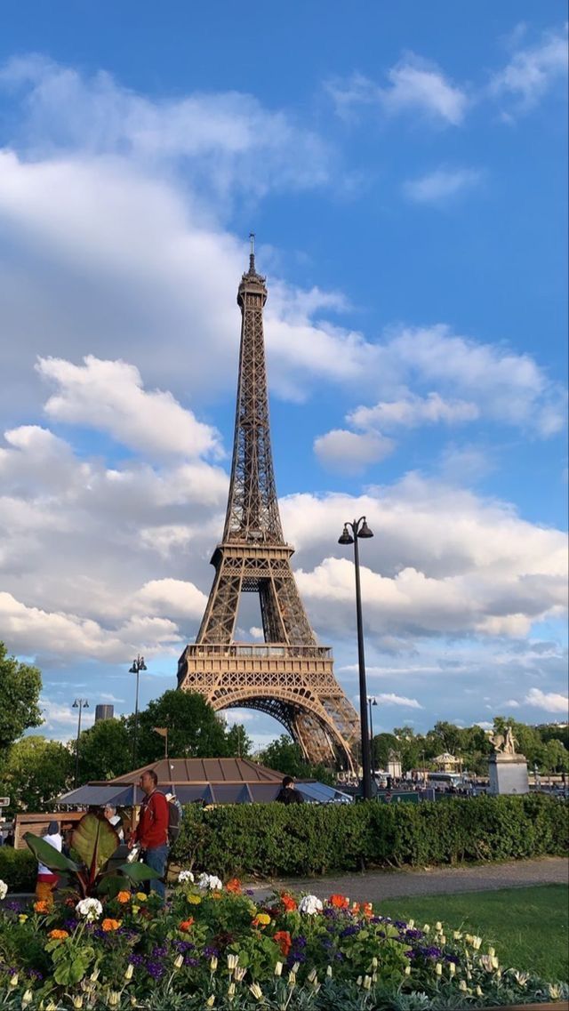 the eiffel tower in paris is surrounded by flowers and greenery, with people standing near it