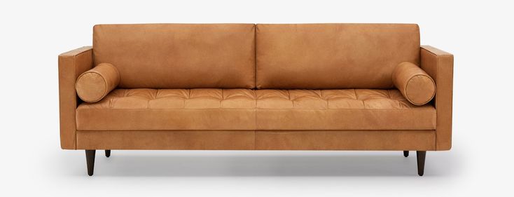 a tan leather couch with wooden legs and armrests on an isolated white background