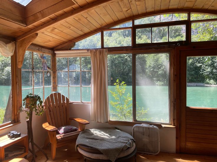 a room with large windows and a chair in front of the window that overlooks a body of water