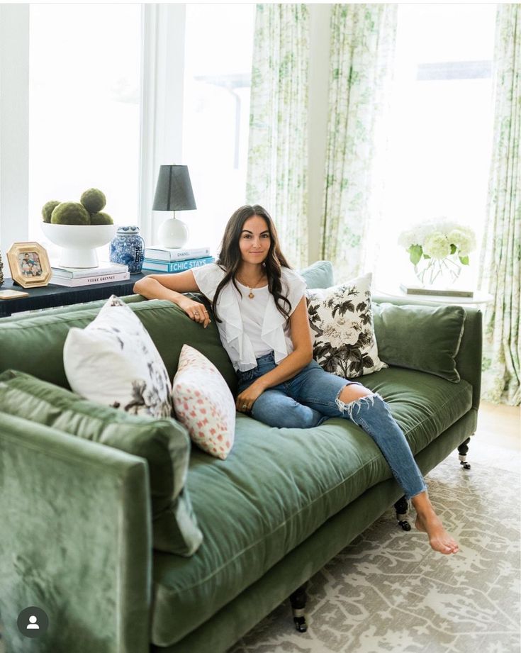 a woman sitting on top of a green couch in a living room next to a window