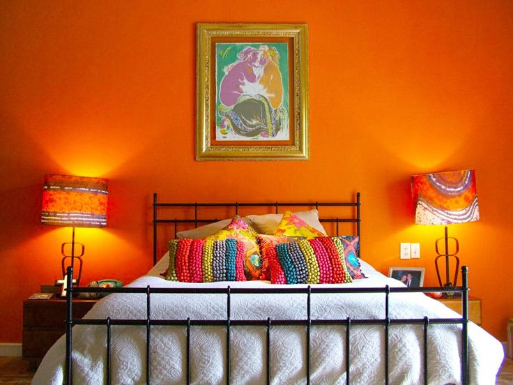 a bedroom with orange walls and white bedding, two lamps on either side of the bed