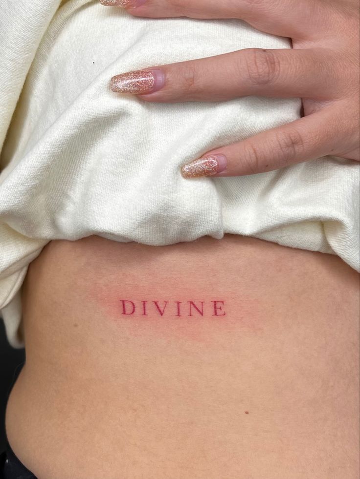 a woman's stomach with the word divine tattooed on it