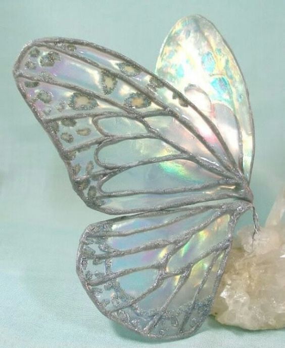 a white butterfly figurine sitting on top of a piece of glass next to a rock