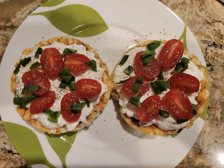 two small pastries are topped with fresh tomatoes and basil on a floral patterned plate