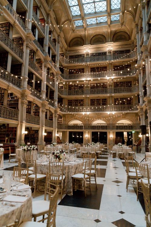 a large room filled with tables and chairs covered in white tablecloths, surrounded by tall bookshelves