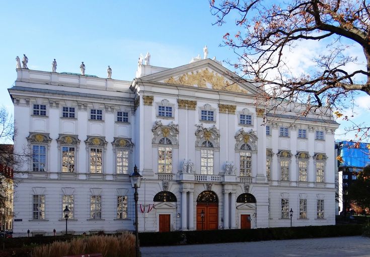 a large white building with red doors and windows on the front side, surrounded by trees