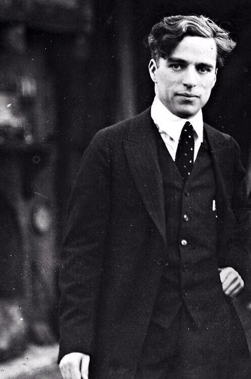 an old photo of a man in a suit and tie walking down the street with his hand on his hip