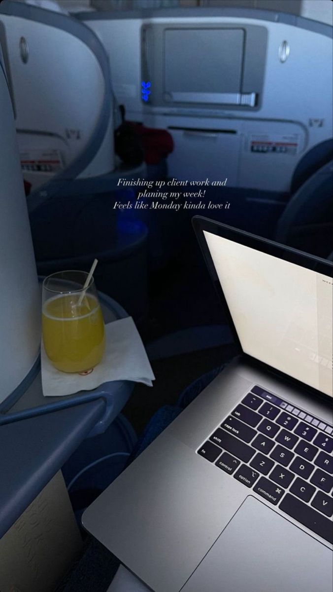 a laptop computer sitting on top of an airplane seat next to a glass of orange juice