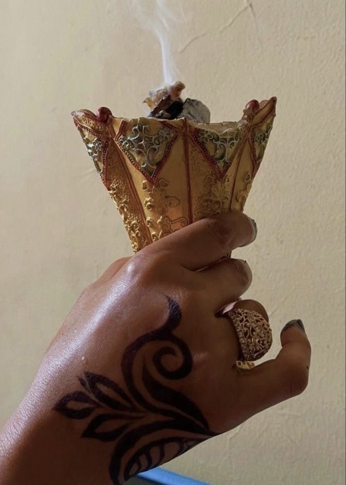 a hand holding a gold crown with tattoos on it