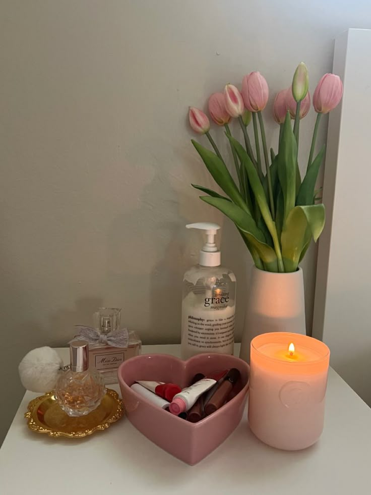 a vase filled with pink tulips next to a candle and some other items