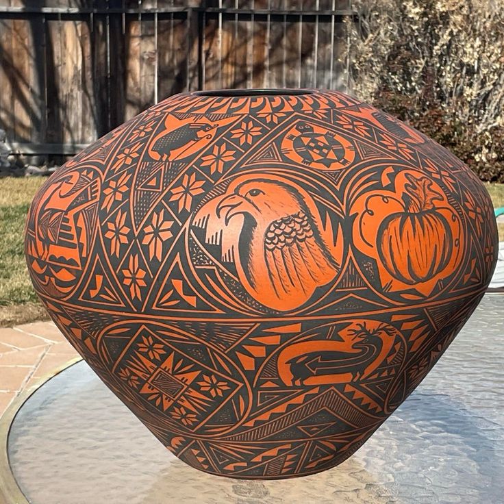 an orange and black vase sitting on top of a glass table in front of a house