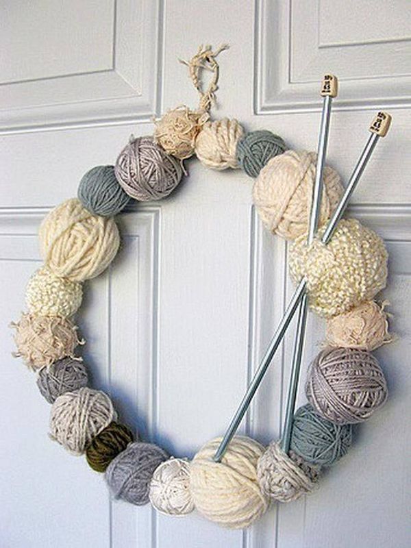 a yarn wreath hanging on the front door with knitting needles and balls of yarn in it