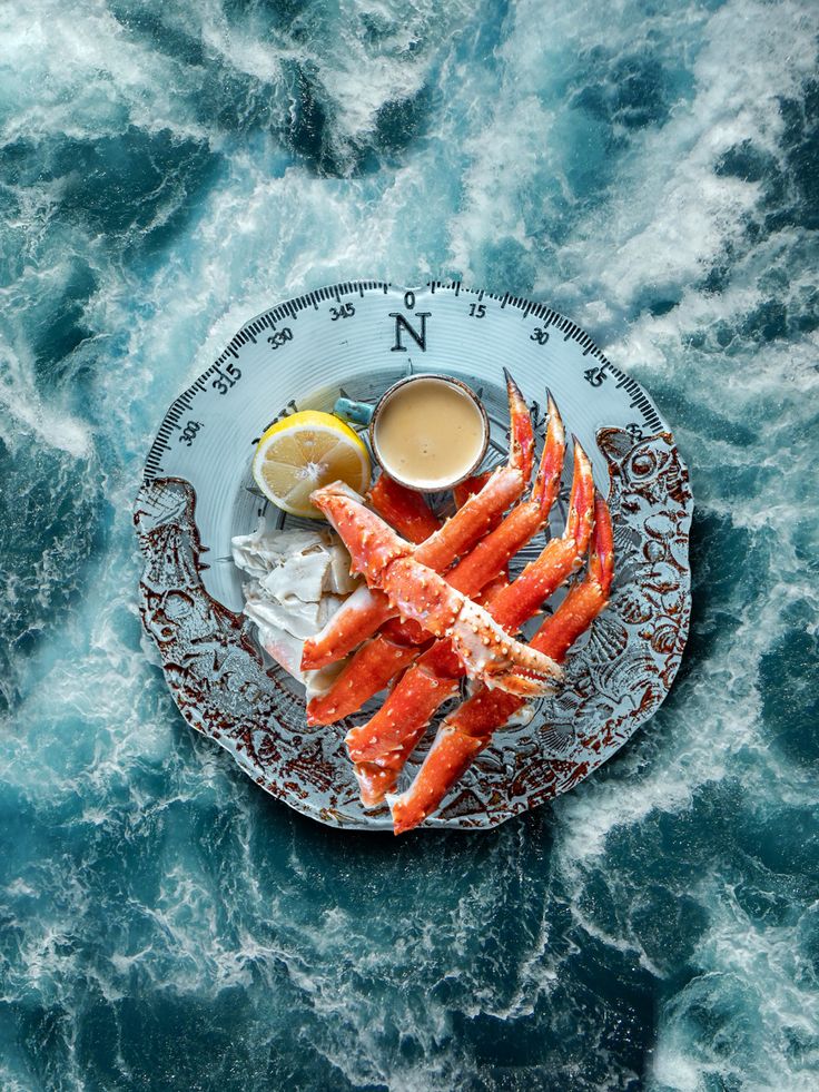 crab legs on a plate with dipping sauce and lemon wedges next to it, surrounded by water