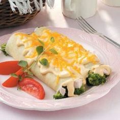 a white plate topped with broccoli and cheese covered enchilada next to a cup of coffee