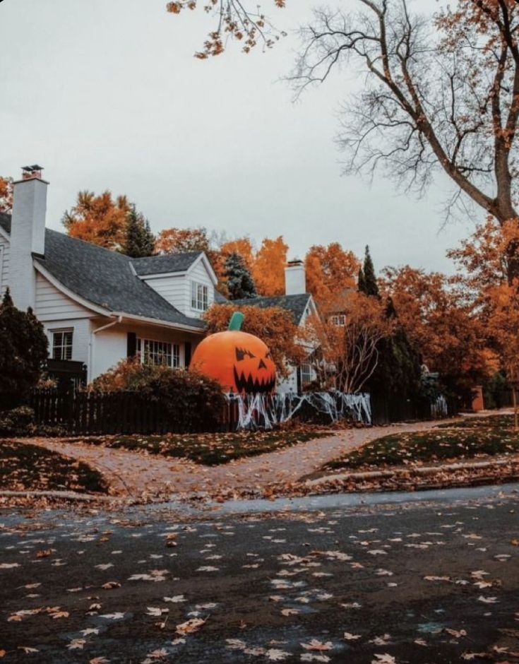 a house decorated for halloween with pumpkins on the front yard and trees around it