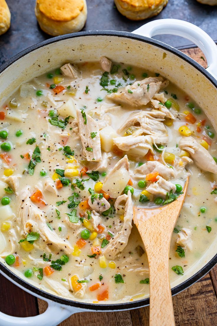 a pot filled with chicken and vegetable soup next to muffins on the side