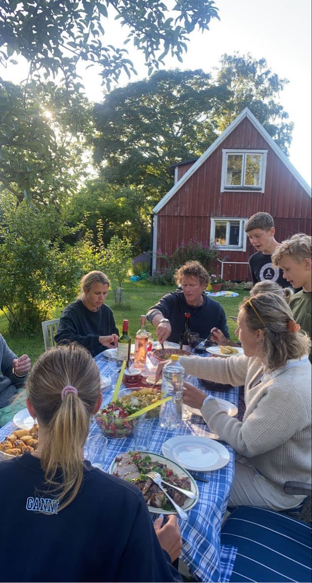 a group of people sitting at a picnic table eating food and drinking wine in front of a red barn