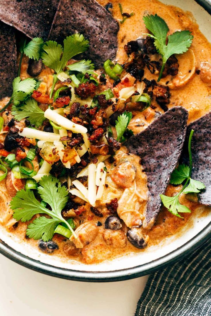 a white bowl filled with food and garnished with cilantro, tortilla chips