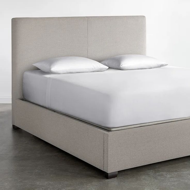 an upholstered bed with white pillows and linens