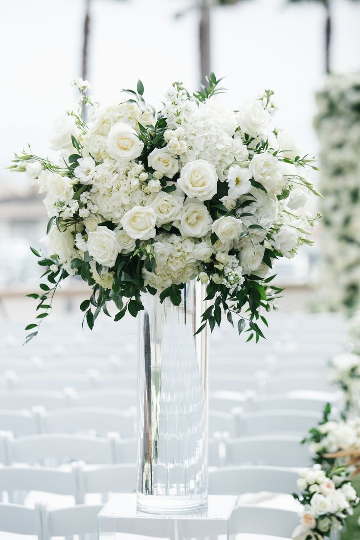 a tall vase filled with white flowers sitting on top of a table next to rows of chairs