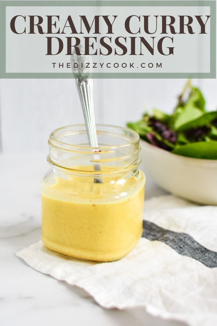 a mason jar filled with creamy curry dressing next to a salad