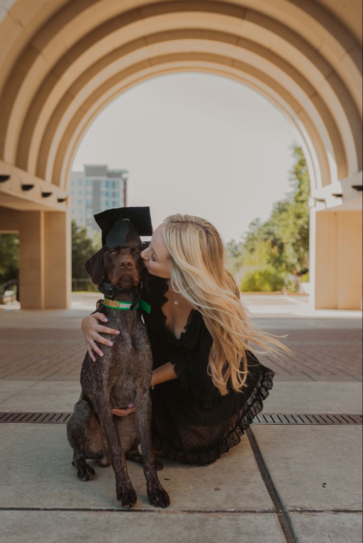 a woman in a graduation cap and gown sitting next to a dog on the ground