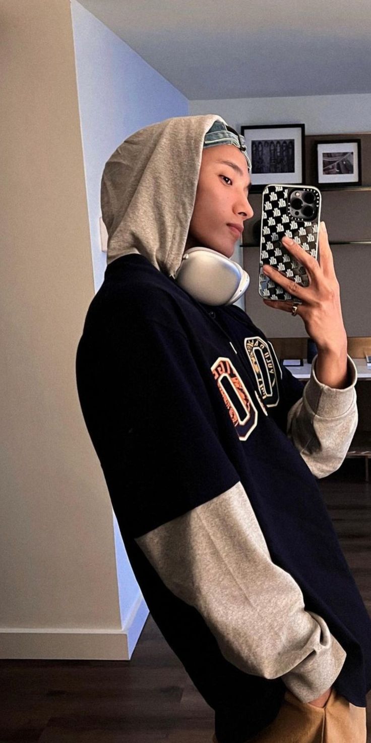 a person in a hoodie holding up a cell phone and wearing headphones on their ears