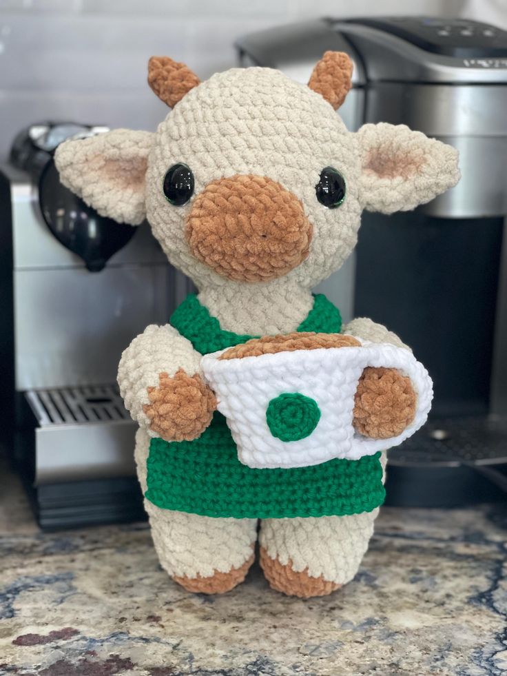 a crocheted stuffed animal holding a coffee cup in front of an espresso machine