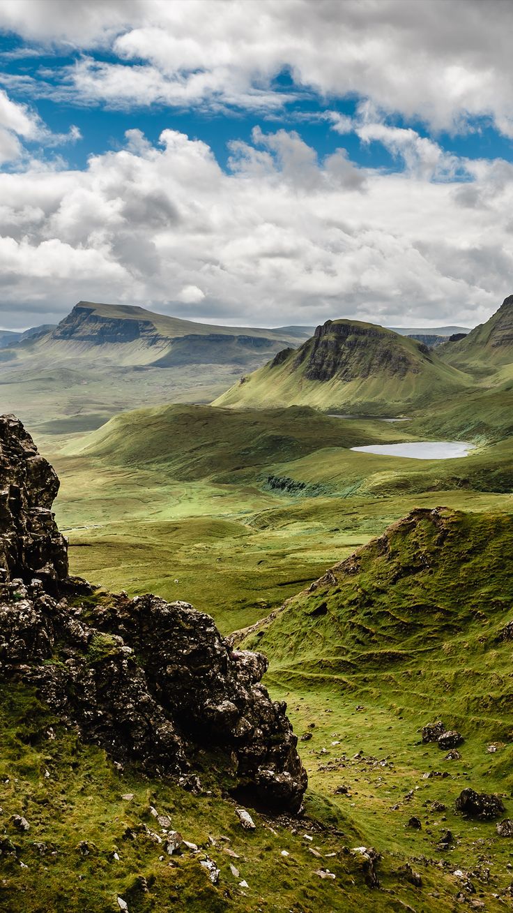 the mountains are covered in green grass and rocks, with a lake on one side