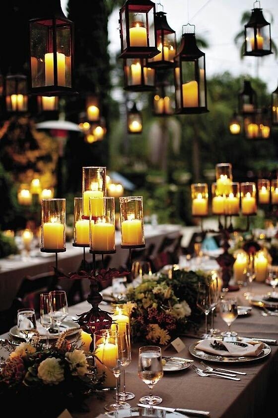 a long table with many lit candles hanging from it's ceiling and place settings