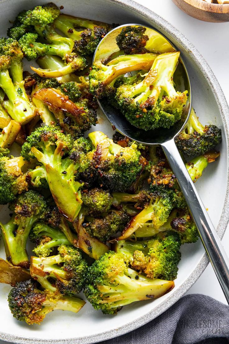 broccoli florets in a white bowl with a spoon on the side