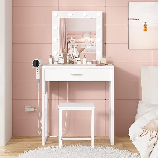 a white vanity table with a mirror and lights on it in a pink walled room