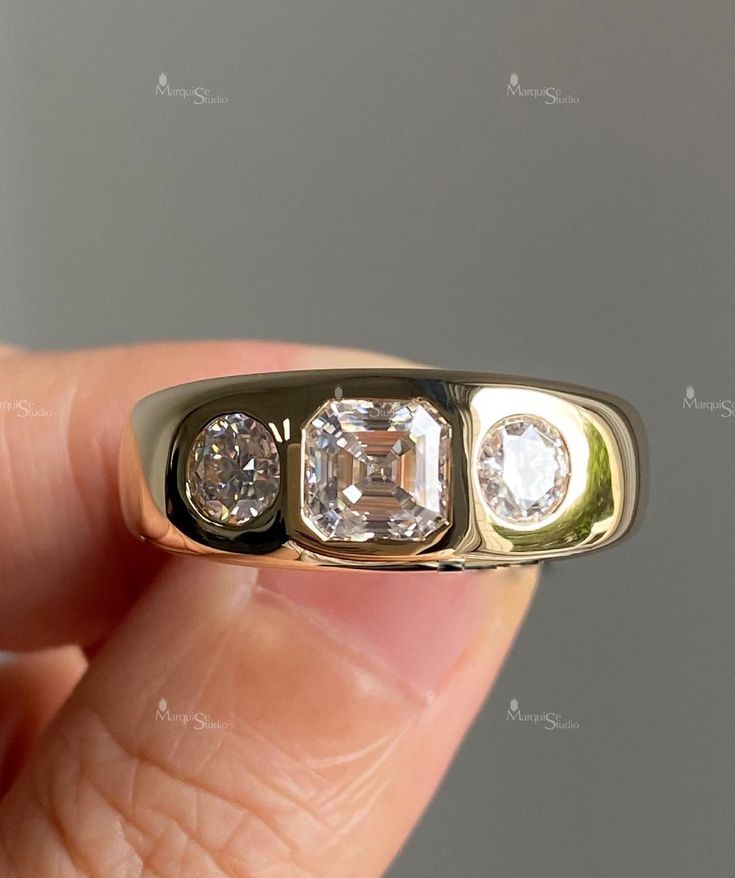 a hand holding a three stone ring in it's left hand, with the center diamond surrounded by four smaller stones