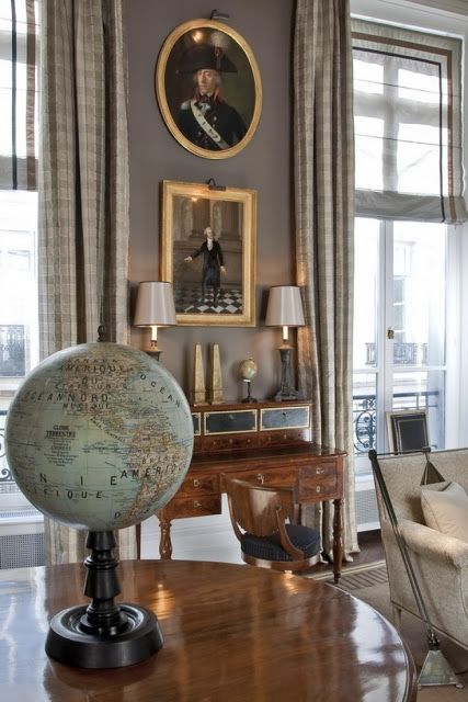 a globe sits on top of a wooden table in front of two windows with drapes