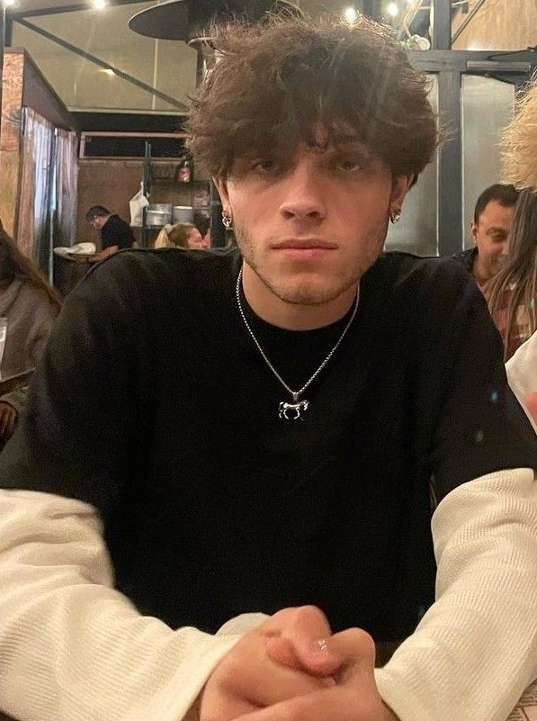 a young man sitting at a table in front of a teddy bear wearing a black shirt