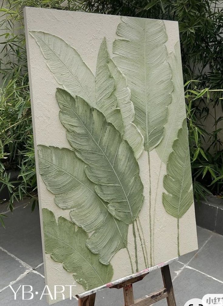 an easel with a painting on top of it in front of some plants and bushes