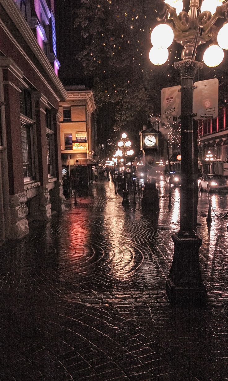 an empty city street at night with lots of lights on the buildings and people walking down the sidewalk