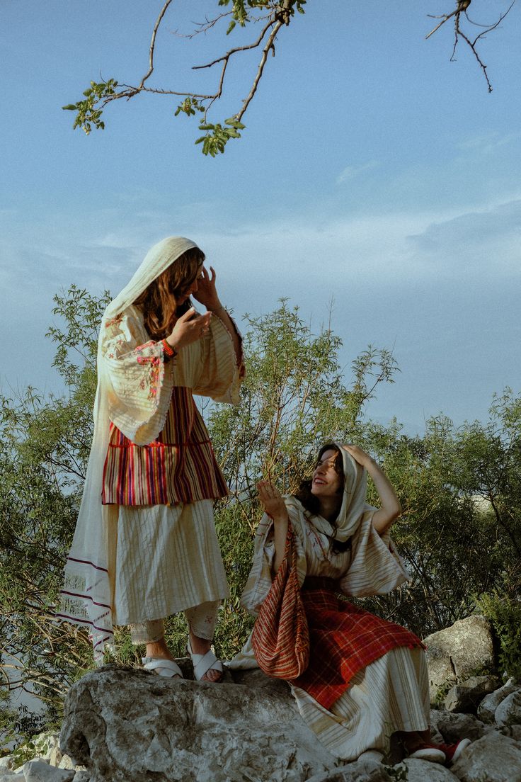 two women dressed in traditional clothing standing next to each other and talking on cell phones