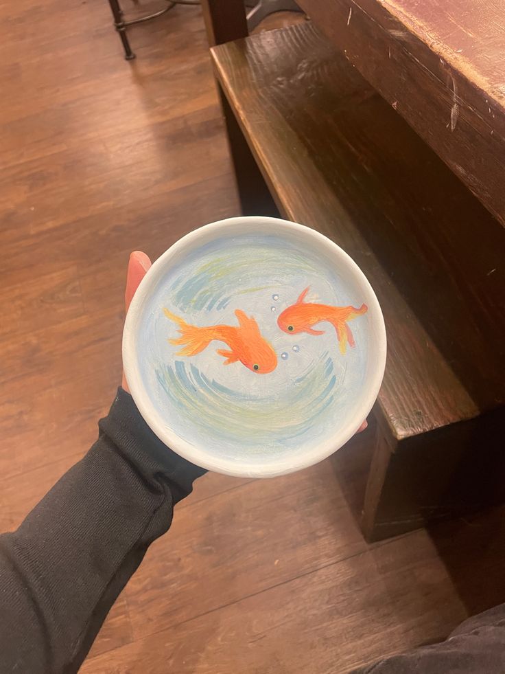 a person holding a bowl with two goldfish in it